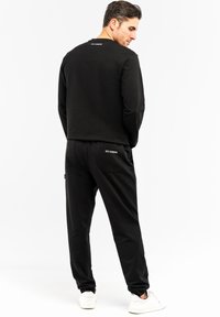 Sort atletisk sæt bestående af en langærmet top og bukser. Toppen har en rund halsudskæring; bukserne har lommer med teksten "ICE ICEBERG". Hvide sneakers.