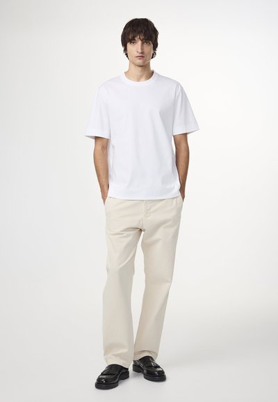 Witte katoenen t-shirt met korte mouwen, gecombineerd met lichtbeige broeken. Zwarte schoenen met een gestructureerd patroon complementeren de outfit.
