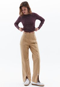Beige wijde broek met ritsen aan de zoom, gecombineerd met een gedempt paarse lange mouwtop met een ronde hals.