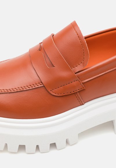 Brune skinn slip-on sko med fremtredende sømmer, en avrundet tå, og en tykk hvit gummisåle med dype spor for grep.