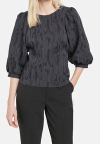 Blusa nera in tessuto con effetto testurizzato, maniche a palloncino e scollatura rotonda, caratterizzata da un sottile motivo astratto. Abbinata a pantaloni neri.