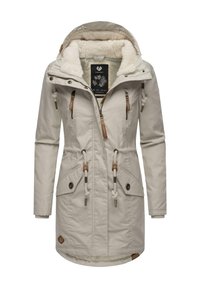 Beige long coat with a plush interior, drawstring waist, zippered and snap button pockets, and faux fur-lined hood.