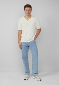 Polo shirt à rayures blanches à manches courtes avec un col en V, associé à un jean droit bleu clair et des baskets grises avec des accents.