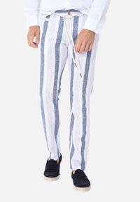 Pantaloni in lino a righe bianche e blu con vita elastica e coulisse, dotati di un dettaglio in legno. Indossati con scarpe nere slip-on.