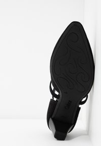 Zwarte suede schoen met een spitse neus en een lage blokhak. Kenmerken van uitgesneden bandjes en een gestructureerde rubberen zool met decoratieve lijnen.