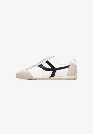 Zapatilla deportiva de cuero blanco con detalles en ante negro y beige, suela plana, cierre de cordones y costuras decorativas a lo largo de los laterales.