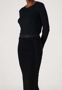 Zwarte lange mouw top met ronde hals, gecombineerd met een aansluitende zwarte rok met een gestructureerde tailleband en zijdetails van gaas.