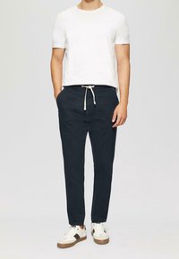 Marineblauwe lichtgewicht broek met een verstelbare tailleband en twee voorzakken, gecombineerd met een effen wit T-shirt en casual sneakers.