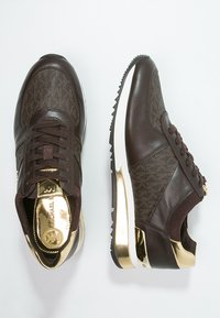 Scarpe sneaker basse marroni e dorate con motivo texturizzato, chiusura con lacci davanti e suola bianca con battistrada nero zigrinato.