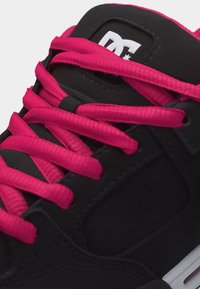 Schwarzer Sneaker mit leuchtend pinken Schnürsenkeln und pinkem Innenfutter, mit einem weißen DC-Logo auf der Zunge.