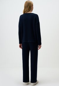 Marineblauer Strickpullover und passende Hose in lässiger Passform. Verfügt über gerippte Textur und lange Ärmel und wird mit weißen Turnschuhen getragen.
