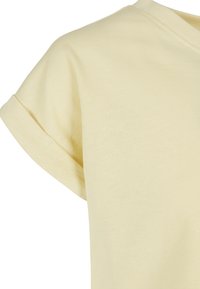 T-shirt di cotone giallo chiaro con maniche corte arrotolate, texture morbida e scollatura a V. Tessuto semplice e privo di decorazioni.