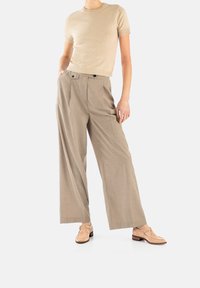 Beiger Strick-Shortsleeve-Top kombiniert mit hellbraunen, weiten Hosen aus strukturiertem Stoff und Doppelknebel-Details. Schuhe in neutralen Farbtönen.