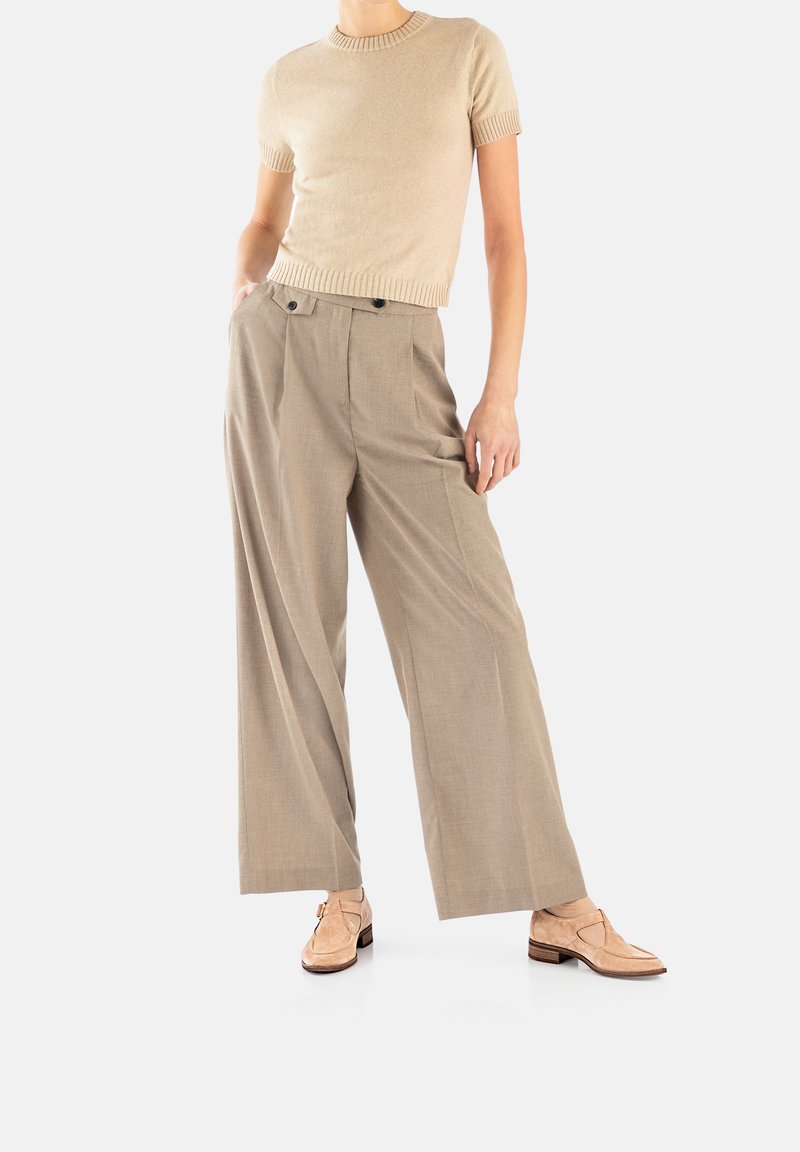 Beiger Strick-Shortsleeve-Top kombiniert mit hellbraunen, weiten Hosen aus strukturiertem Stoff und Doppelknebel-Details. Schuhe in neutralen Farbtönen.