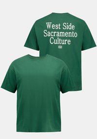 Camiseta de algodón verde con mangas cortas, cuello redondo y texto en la parte de atrás que dice "Cultura del West Side de Sacramento" en blanco.