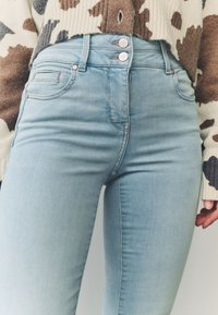 Svjetloplave uske traperice s visokim strukom, s tri metalna gumba i klasičnim dizajnom s pet džepova. Meka tekstura trapera s diskretnim blijeđenjem.