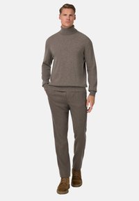 Brązowy sweter z golfem wykonany z miękkiej tkaniny, zestawiony z fakturowanymi brązowymi spodniami. Model nosi brązowe zamszowe buty, prezentując skoordynowany wygląd.