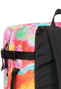 Un sac à dos multicolore avec un motif abstrait vibrant, fabriqué en tissu durable avec une sangle noire et un détail de poche sur le côté.
