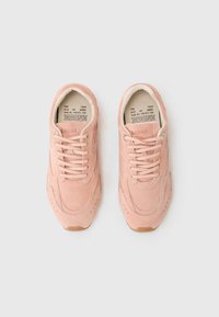 Baskets en daim rose clair avec des détails usés, un design à lacets et une semelle en caoutchouc avec une subtile marque à l'intérieur.