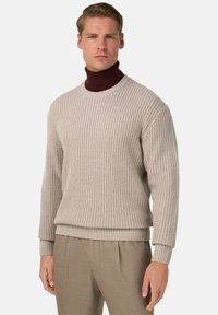 Pull en maille beige avec un motif texturé, col rond et poignets côtelés. Associé avec un pantalon marron clair.