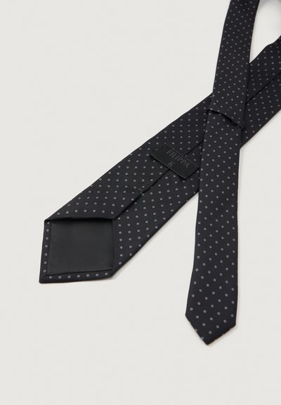 Cravatta in seta nera con un discreto motivo a pois grigio chiaro, posata piatta per mostrare l'etichetta interna e i dettagli della cucitura.