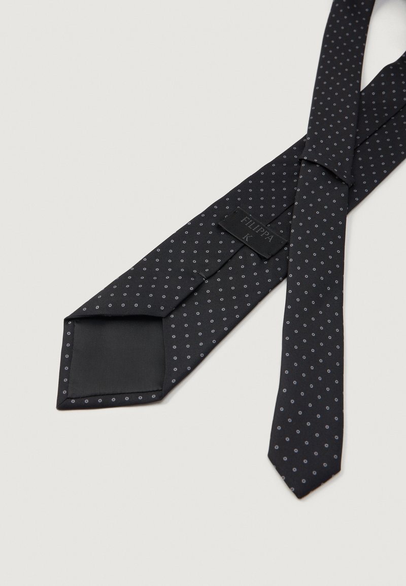 Schwarze Seidenkrawatte mit einem subtilen, hellgrauen Punktmuster, flach ausgelegt und zeigt das innere Etikett sowie die Nähdetails.