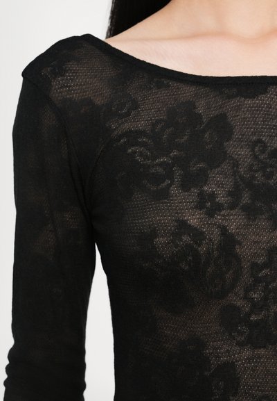 Svart mesh topp med lange ermer og vid hals, med et blomstermønster som svakt vises gjennom det gjennomsiktige stoffet.