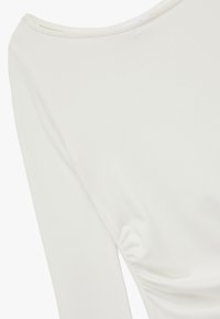 Hvid langærmet bluse med en bred krave, glat tekstur og sammensyning på siden for en tætsiddende silhuet.