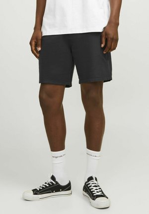 Sorte bomuldsshorts med elastisk talje, midt på låret, parret med hvide ankelstrømper og sorte canvas sneakers.