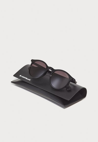 Black sunglasses with round lenses, featuring a glossy frame, resting on a black leather case with a white logo.