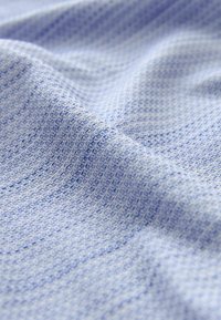 Tissu bleu clair avec un motif à grille finement texturé, présenté avec des plis doux et des ombres délicates.