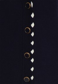 Marinblå stickad kofta med guldfärgade knappar och vita diamantformade detaljer längs knappslån, vilket skapar en texturerad detalj.