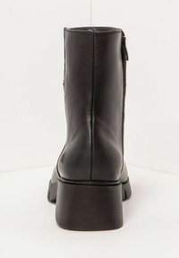 Botín negro de piel con puntera cuadrada y tacón cuadrado, que cuenta con una cremallera lateral y una textura suave. Diseño minimalista y perfil elegante.