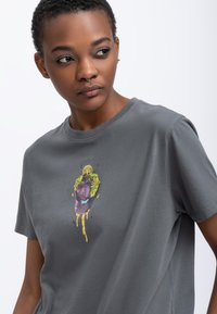 Grijze katoenen t-shirt met een kleurrijke grafische print van een personage met een groene bladeren kroon, ontworpen met een ronde halslijn en korte mouwen.