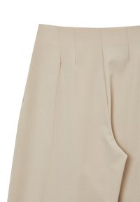 Beige Hochbundhose mit Frontfalten und seitlichem Taschendetail aus glattem Stoff.