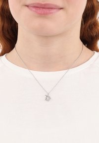 Collana in argento con charm a forma di unicorno, caratterizzata da dettagli intricati e una finitura lucida, indossata sopra una camicia bianca.