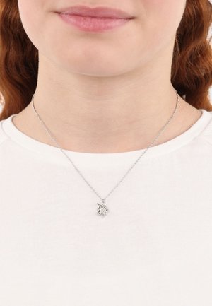 Collana in argento con charm a forma di unicorno, caratterizzata da dettagli intricati e una finitura lucida, indossata sopra una camicia bianca.