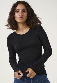 Top nero a maniche lunghe realizzato in tessuto liscio, con collo rotondo, design aderente e maniche leggermente arricciate, abbinato a jeans blu.