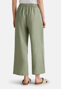 Pantalones de lino verdes de pierna ancha con una cinturilla elástica. Textura suave y corte holgado. Combinados con sandalias planas beiges con detalles de piel.