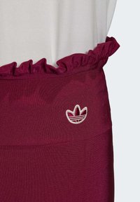 Burgundy kjol med volangmidja och vit broderad Adidas-logotyp på översidan, tillsammans med en vit topp.