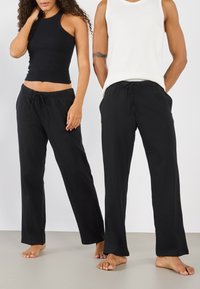 Pantalons de lounge noirs avec un waistband élastique et un cordon de serrage, associés à des hauts sans manches noirs et blancs ajustés sur deux modèles.