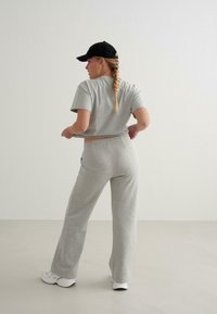 Grå bomulds T-shirt med korte ærmer og matchende sweatpants med en afslappet pasform, suppleret med en sort baseball cap og hvide sneakers.