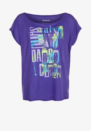 Fioletowa bawełniana koszulka o luźnym kroju i krótkich rękawach. Zawiera wyraźny, wielokolorowy napis: "To nie jest lekcja tańca." Obecne logo Reebok.