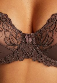 Rjav čipkast modrček z cvetlično vezenino, prosojnimi mrežastimi detajli in satenastim lokom na sredini. Gladek material z oblikovano zasnovo.