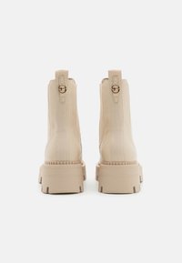 Botines beige con un acabado de piel suave y paneles laterales elásticos. Suela de plataforma gruesa con bordes estriados y acentos de hardware redondeados.