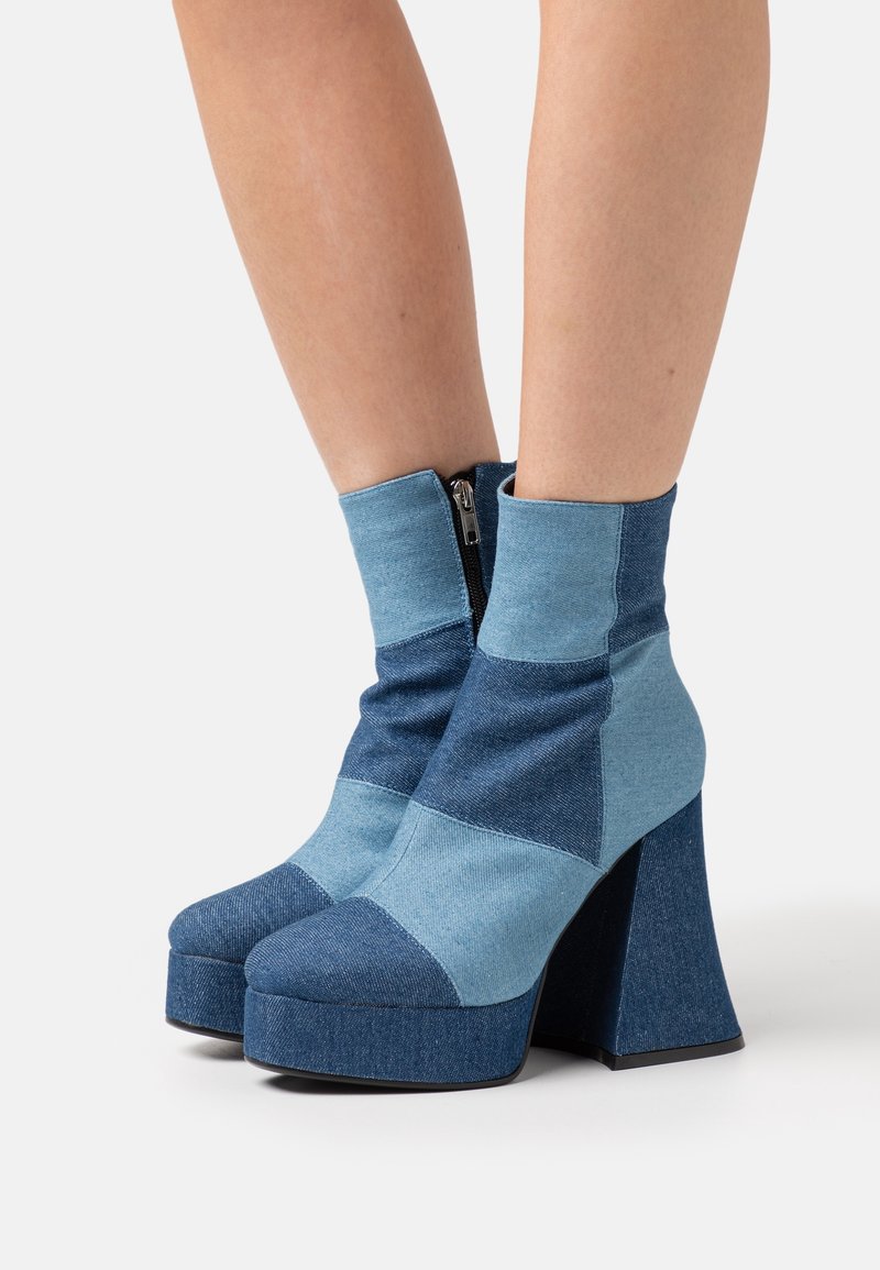 Bottes cheville en denim avec un design patchwork dans différentes nuances de bleu, talon bloc haut et fermeture éclair à l'avant pour un enfilage facile.