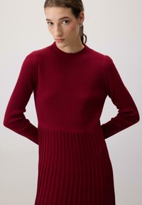 Burgundi színű bordázott ruha hosszú ujjal, testhez simuló felső résszel és bő szoknyával. Puha tapintású, magas nyakú, finom övpánt részlettel.