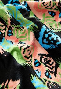 Multikleurige stof met abstracte patronen in roze, groen, zwart en blauw. Gladde textuur met een glanzende afwerking.