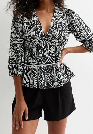 Blusa de estampado en blanco y negro con escote en V profundo, cintura elástica y mangas de tres cuartos, combinada con pantalones cortos negros.