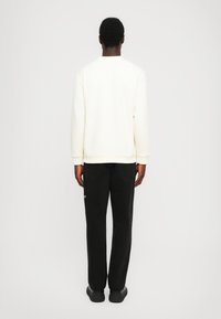 Cream sweatshirt with long sleeves, ribbed cuffs, and hem; paired with black jeans and black shoes. View from the back.